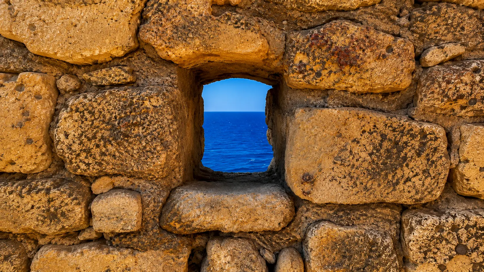 Finestra tra antiche pietre affacciata sul mare blu di Milos, in Grecia